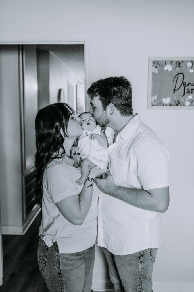 Parents holding newborn in softly lit bedroom during dreamy lifestyle session