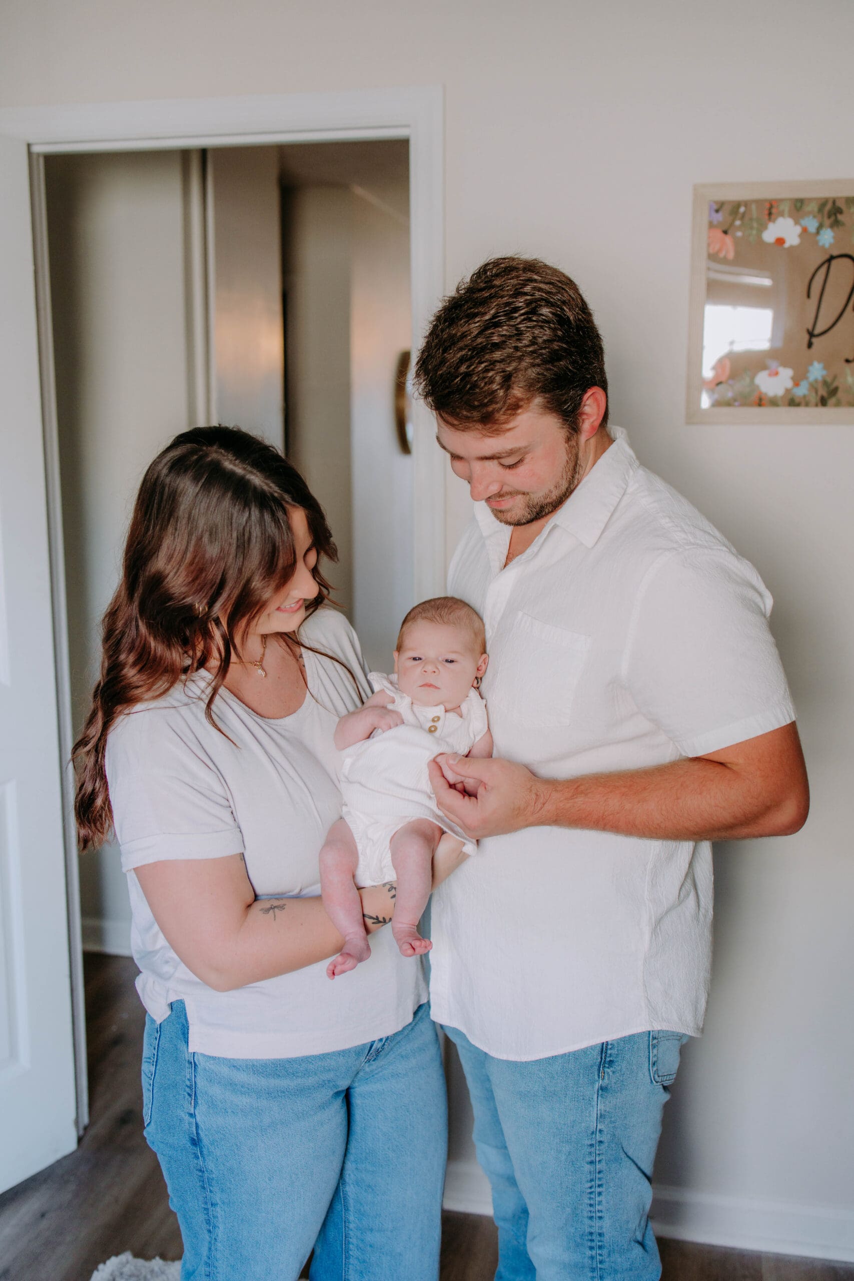 Parents holding newborn in softly lit bedroom during dreamy at-home lifestyle session