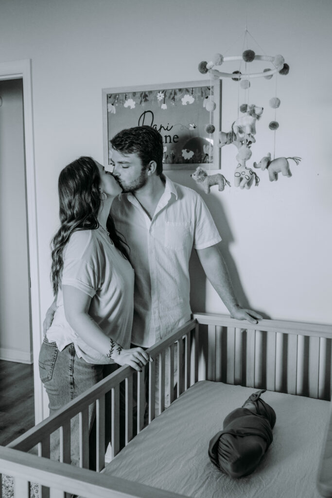 Parents holding newborn in softly lit bedroom during dreamy lifestyle session