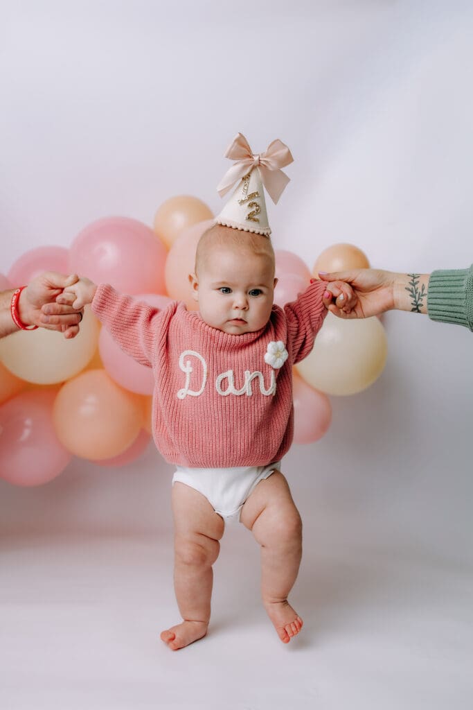 6 month baby standing with parents hands for milestone photoshoot